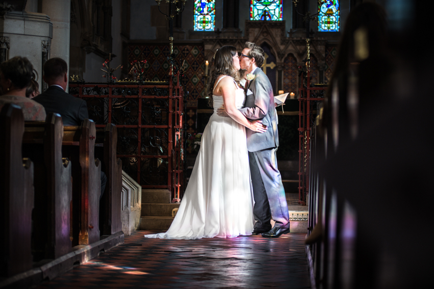 Stain glassed lighting hits Groom during first kiss.